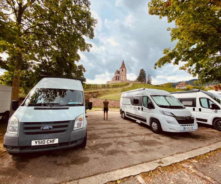 Parking lot with vans in Hunawihr; Saint-Jacques-le-Majeur church in background