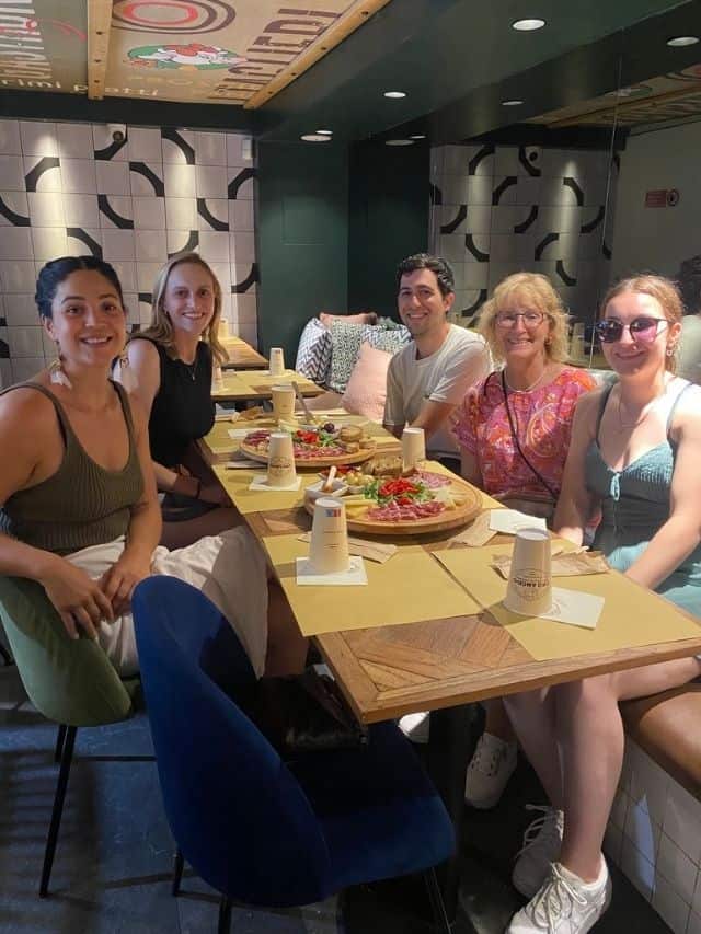 Five people sitting around a table smiling at camera with two large antipasto platters central on table.
