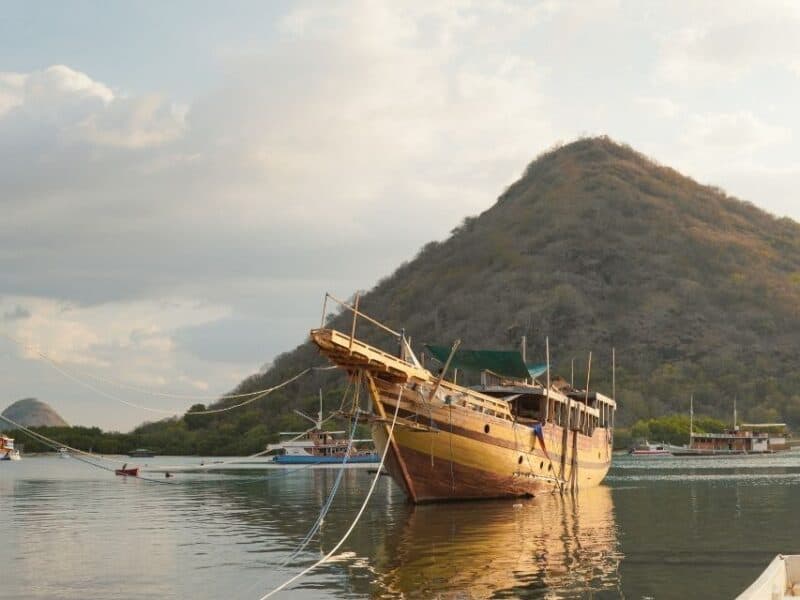 Traditional wooden boat anchored in Labuan Bajo harbour with dry hills in the background