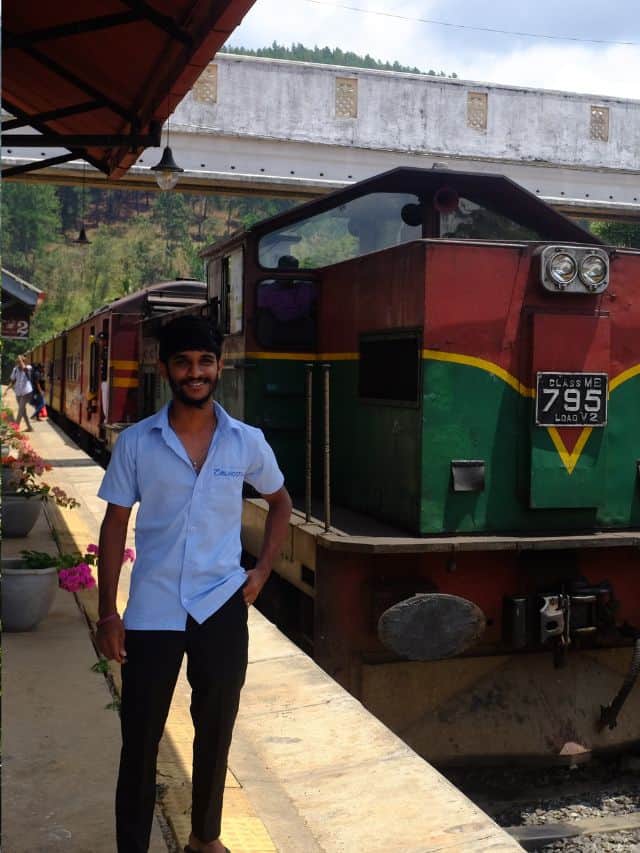 Train waiting at Demodara station platform with a local railway worker
