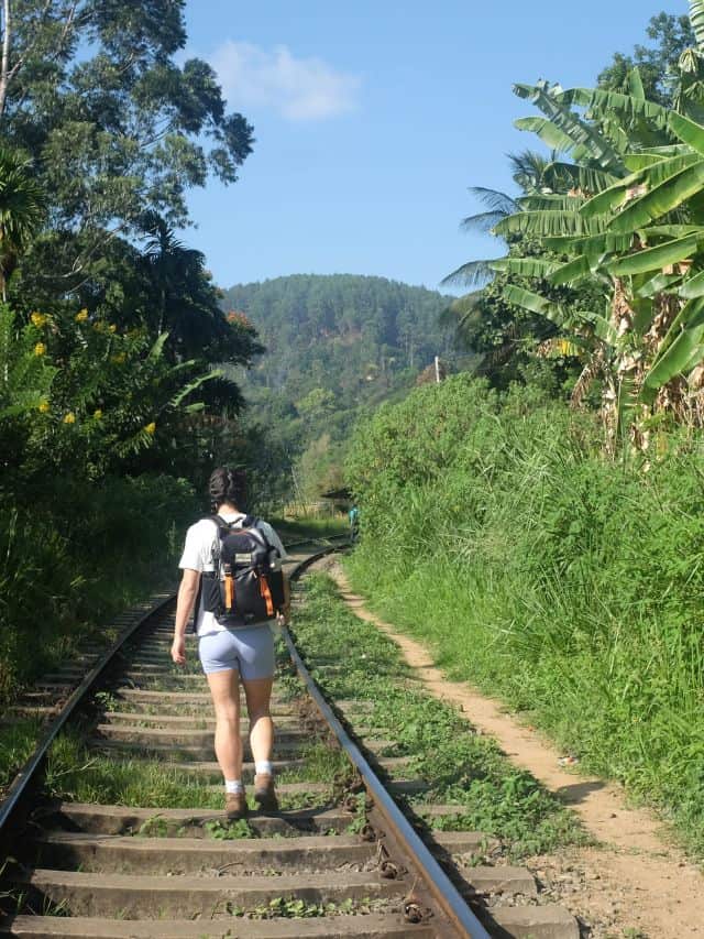 Traveller walking along the railway tracks at the start of the hike near Ella, surrounded by tropical greenery.