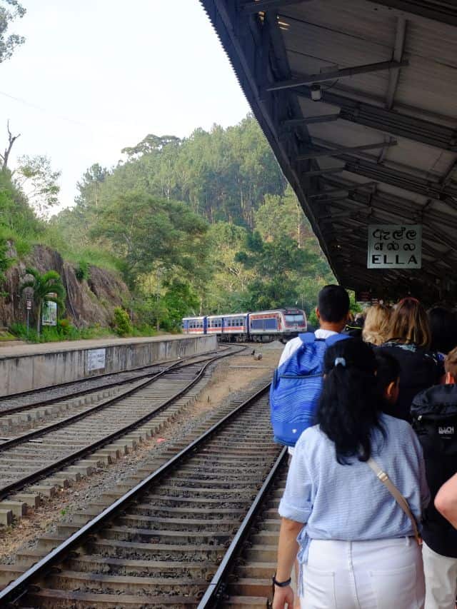 People waiting at Ella railway station with the train curving in through the hills.