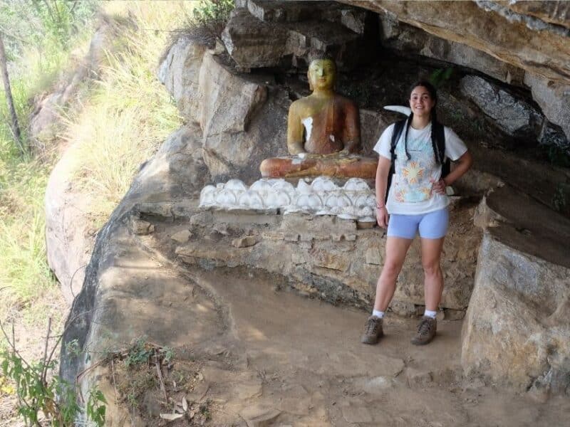 Traveller standing beside a small Buddha statue in a rock shelter near the Ella viewpoint.