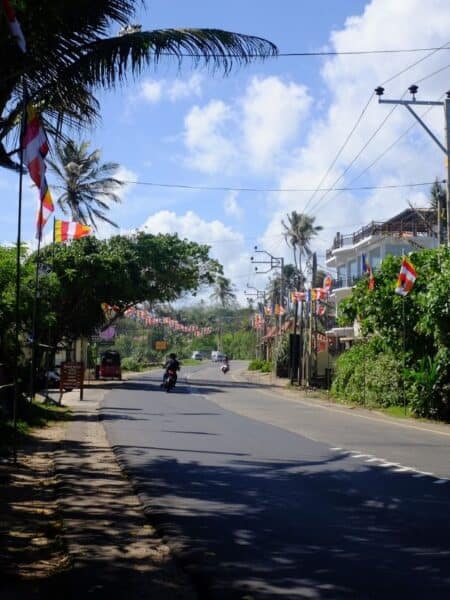 Quiet coastal road in Ahangama Sri Lanka with palm trees, Buddhist flags and scooters under a blue sky