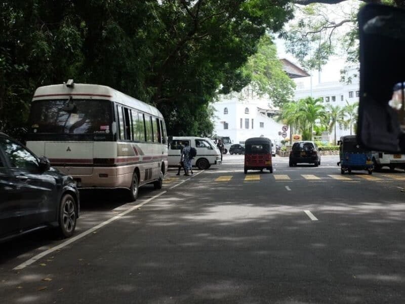 Traffic and tuk-tuks on a shaded road in Sri Lanka, showing everyday transport between towns.