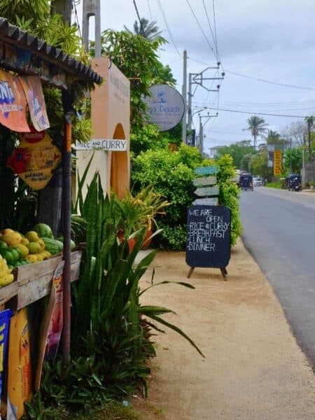 Fruit stall and roadside café sign along a leafy road in Ahangama.