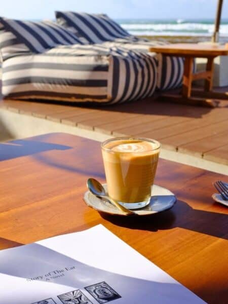 Coffee on an oceanfront café table in Ahangama with sun loungers and waves behind — is Ahangama worth visiting for cafés?