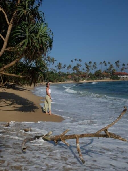 Traveller standing on Dickwella Bay Beach in Sri Lanka with waves washing over the sand and palm trees in the background