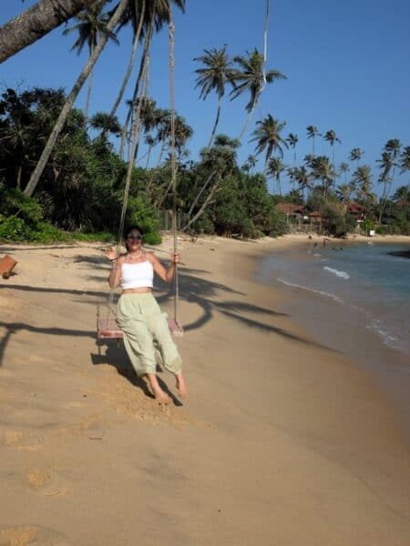 Traveller sitting on a beach swing beneath palm trees on Sri Lankaโs south coast