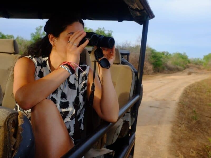 Traveller looking through binoculars from an open safari jeep in Udawalawe National Park, Sri Lanka