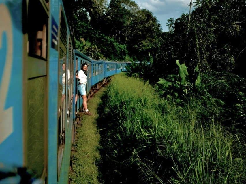 Traveller leaning from the blue train during the scenic Kandy to Ella train journey in Sri Lanka.