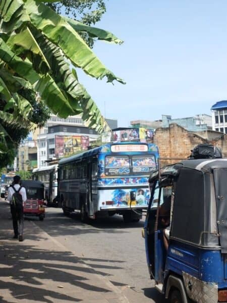 Colourful local bus and tuk-tuks on a busy Sri Lankan street.
