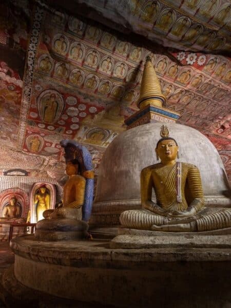 Buddha statues and painted cave ceiling inside Dambulla Cave Temple in Sri Lanka.
