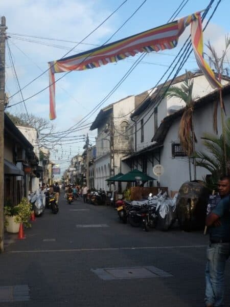 Quiet colonial street in Galle Fort with Buddhist flags, old buildings and parked scooters.