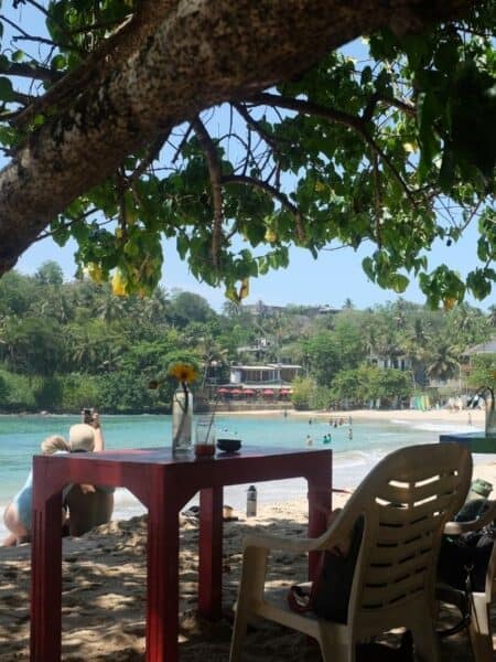 Beach café table under the trees overlooking Hiriketiya Bay in Sri Lanka.