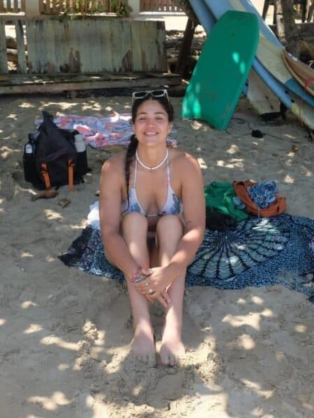 Traveller sitting on the sand at Hiriketiya Beach with beach bags and surfboards nearby.