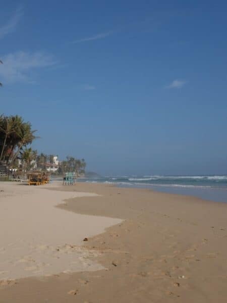 Wide sandy Kabalana beach with gentle waves and palm trees on the south coast of Sri Lanka.