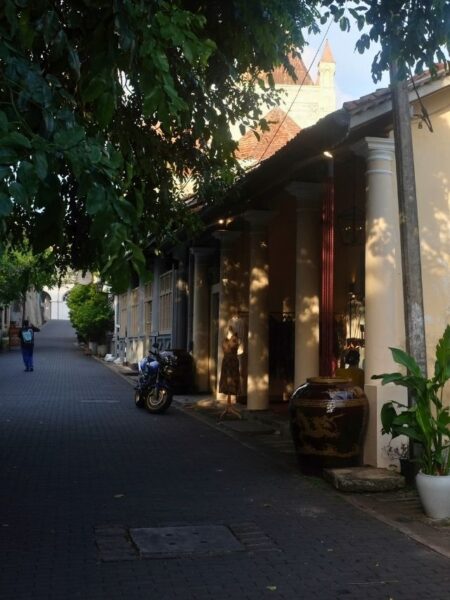 Shaded colonial lane inside Galle Fort with old buildings, trees and warm evening light.