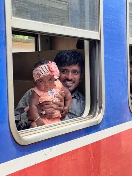 Man holding a baby at the window of a blue Sri Lankan train during a Sri Lanka 5 days itinerary.