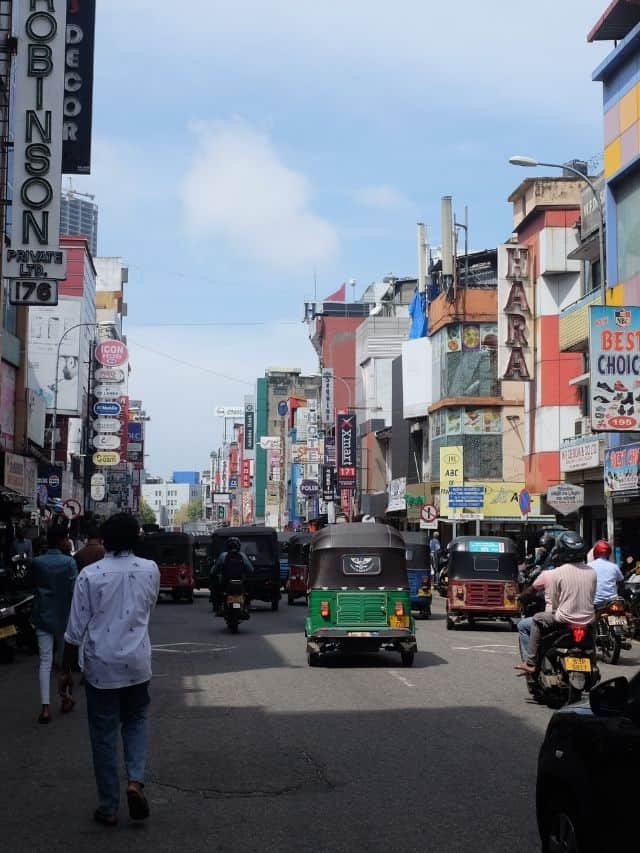 Busy Colombo street with tuk-tuks, shops and traffic during a city tour